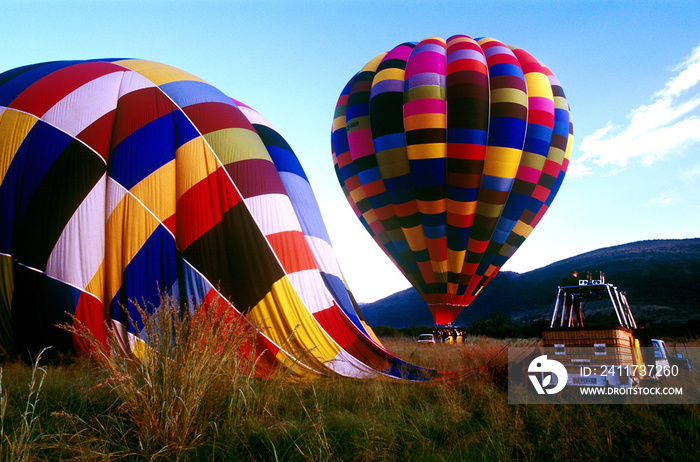 aerostatic balloons  one inflating with a flying basket next to it and a second inflatable balloon with a basket and people ready to fly