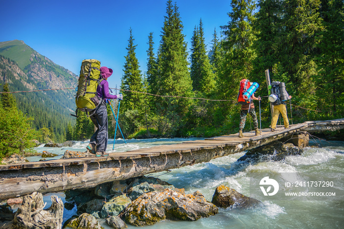 Hikers crossing over wood bridge under mountain river.