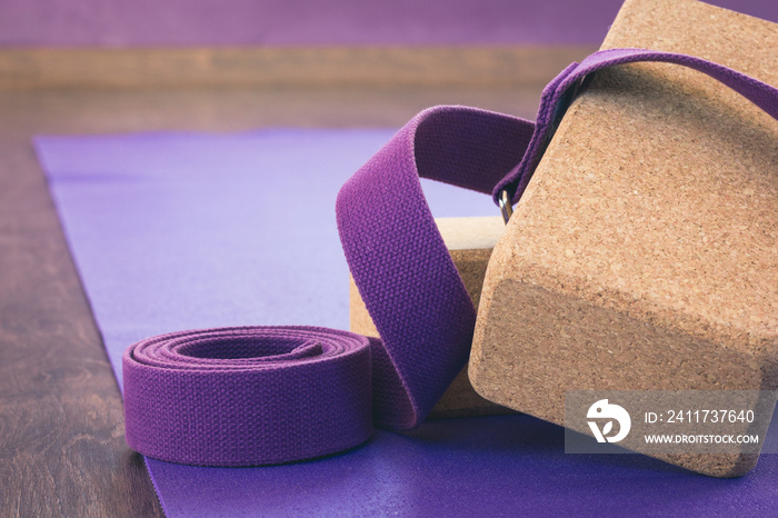 Yoga studio props. Cork bricks, purple strap and mat on wooden floor