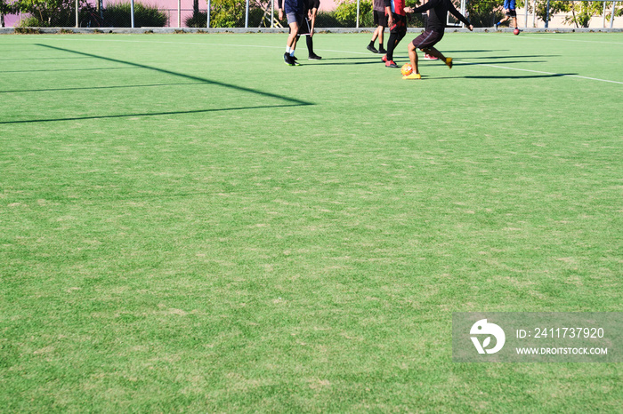 Unrecognizable young men play soccer on a synthetic grass field on a sunny day