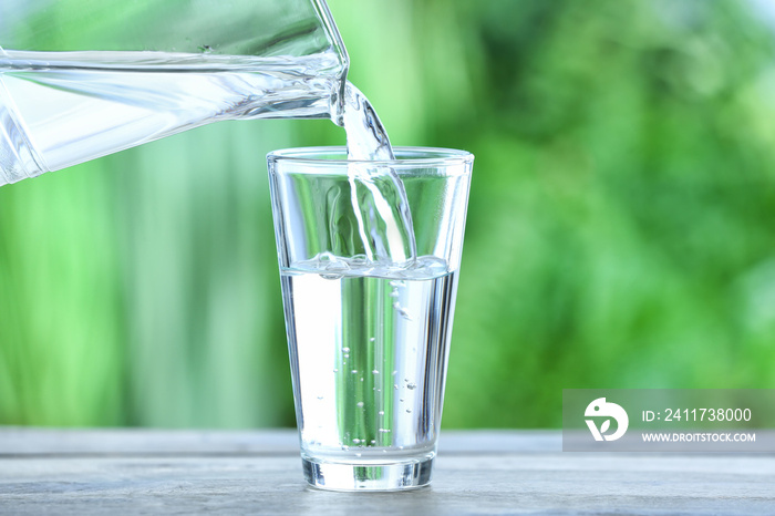 Pouring of fresh water into glass on table outdoors