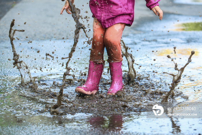 Playful child outdoor jump into puddle in boot after rain