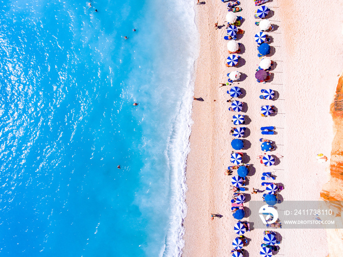 Top down view of a beach with tourists suntbeds and umbrellas with sand beach and clear blue water in Greece