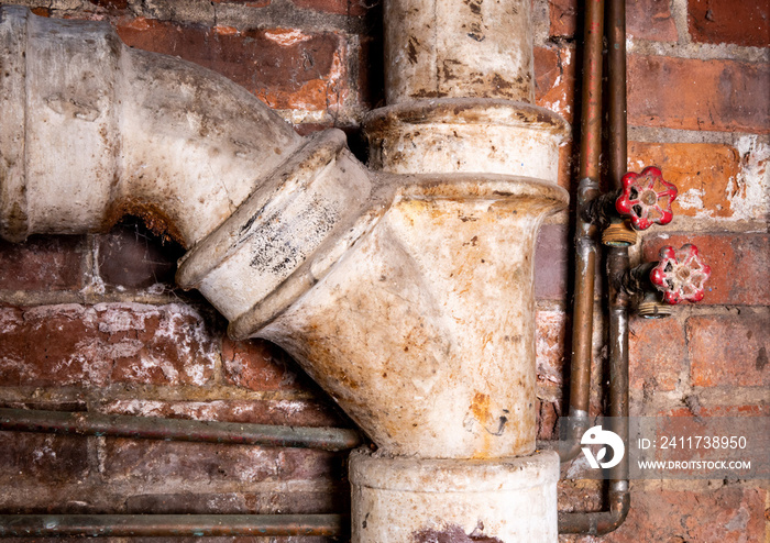 corroded laundry tub water supply valves and a rusty sewer drain pipe in a grungy basement