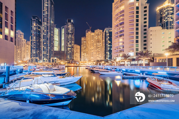 yacht and motor boats parking at night in the port near Dubai Marina Mall with row of high skyscrapers residential buildings and hotels