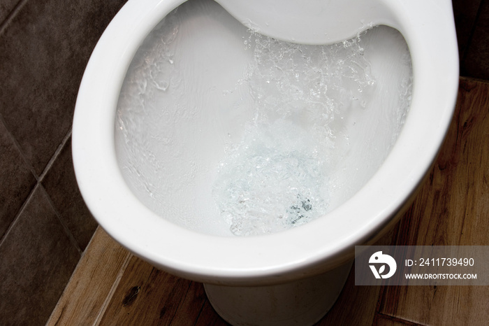 Toilet while flushing urine with water. A stream of water in the toilet bowl