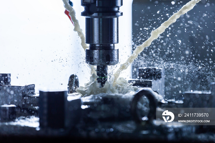 Close-up view of vertical cnc steel milling process with external water coolant streams, splashes and a lot of metal chips, high contrast