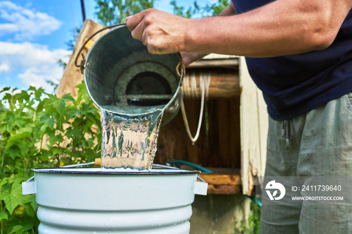 Man pouring water just taken up from a well into a enameled bucket