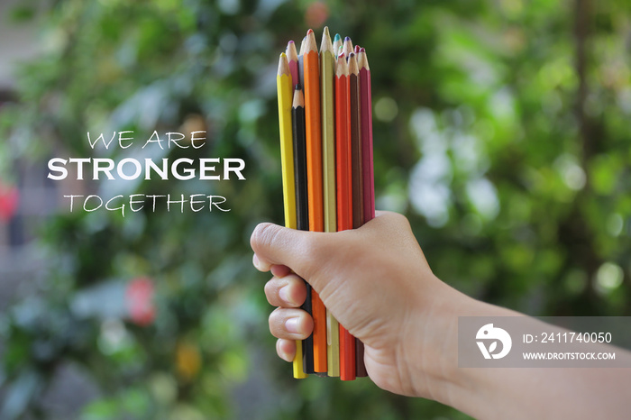 Inspiratinal motivational quote - We are stronger together. With young woman hand holds bunch of pencil colored and blurry green garden background. Togetherness concept.