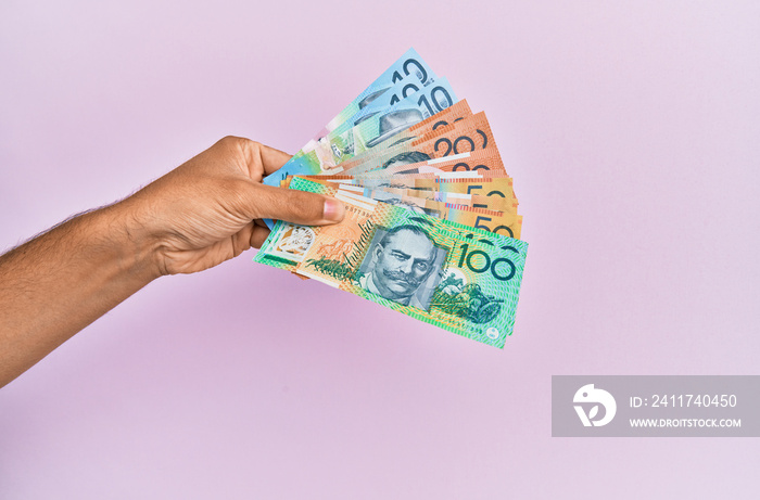 Hispanic hand holding australian dollars banknotes over isolated pink background.