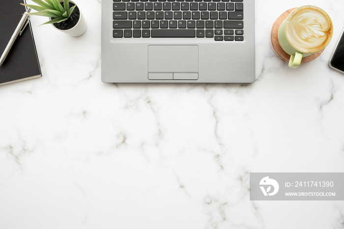 White marble office desk table with laptop computer, cup of latte coffee and office supplies. Top view with copy space, flat lay.