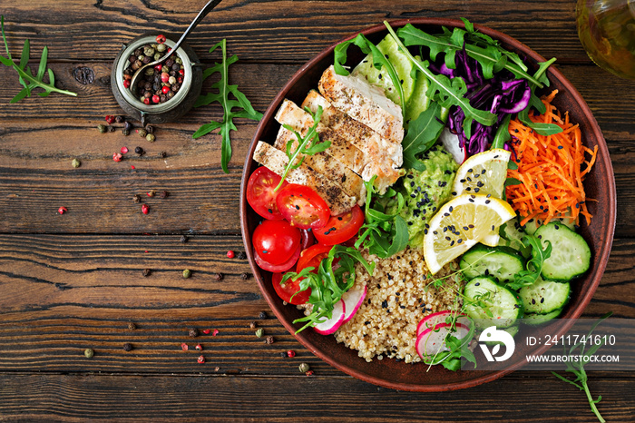 Healthy dinner. Buddha bowl lunch with grilled chicken and quinoa, tomato, guacamole, carrot, red cabbage, cucumber and arugula on wooden background. Flat lay. Top view