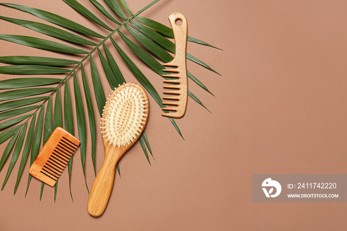 Hair brush, combs and palm leaf on color background