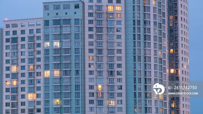 Apartment building windows at dusk. Evening outdoor view of living house facade with warm illumination light. Architecture, urban concept