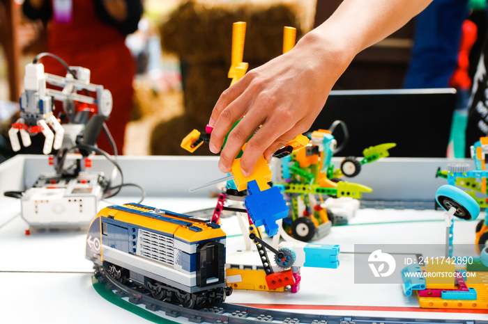 Defocus children hands holding ready made robots on table. Train an railway. Joyful smart whizzkid experimenting with humanoid robotic hand while developing his skills. Coding school. Out of focus