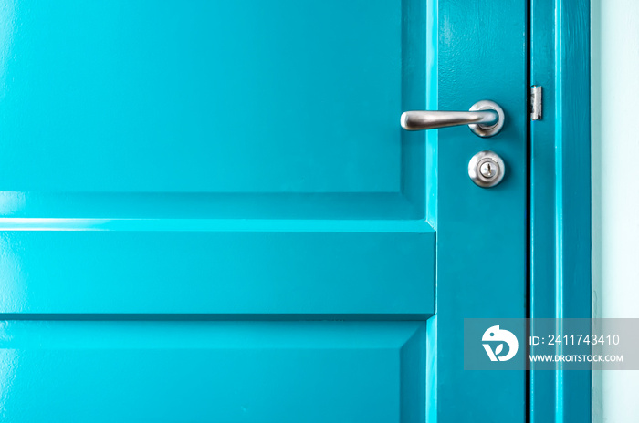 Closed solid wooden door is painted in bright blue with a beautiful metal handle and lock.