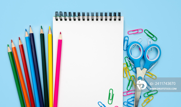 A white blank notebook and colorful school stationery on a blue background. Mockup. Flatlay. Top view. Copy space.