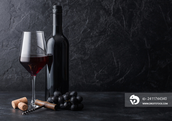 Elegant glass and bottle of red wine with corks and corkscrew on black stone background. Natural Light