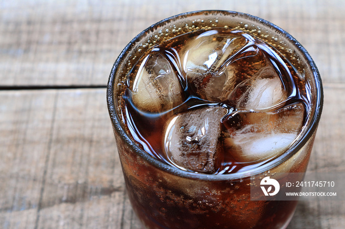 A glass of cola with ice on wood table.