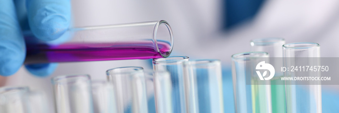 A male chemist holds test tube of glass in his hand overflows a liquid solution of potassium permanganate conducts an analysis reaction takes various versions of reagents using chemical manufacturing