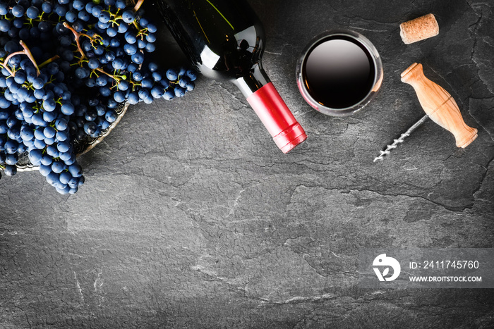 Red wine bottle and full glass, grapes on dark stone table top view. Vine concept on black background.