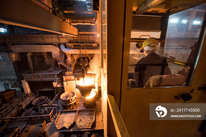 Worker operates in the cabin of a cargo crane at the steel mill