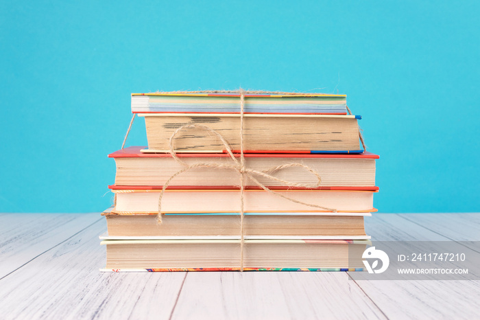 Stack of books and pink heart. Books with jute ribbon bow as gift on blue background. Education background with copy space, back to school concept