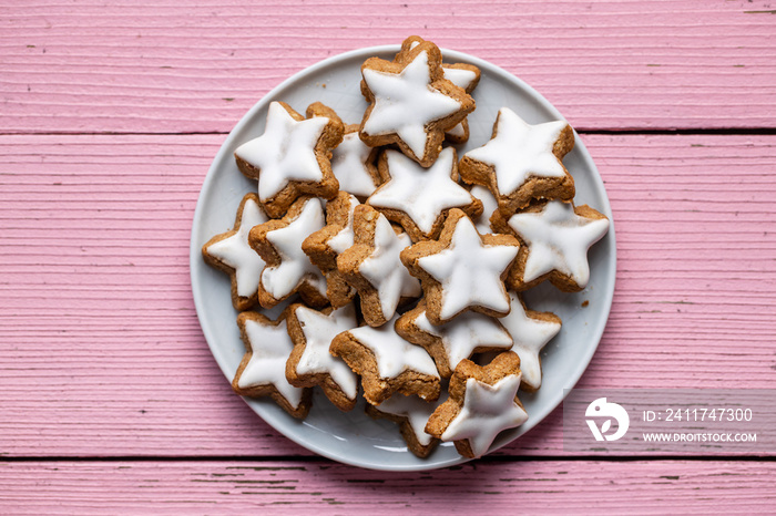 Icing gingerbread stars. Traditional Christmas cookies on pink wooden table.