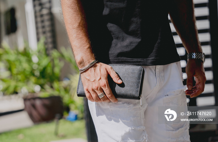 Young businessman holding wallet in his hands against his modern home with garage and car