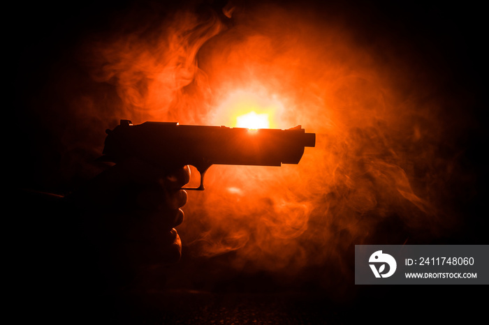 Male hand holding gun on black background with smoke toned back lights