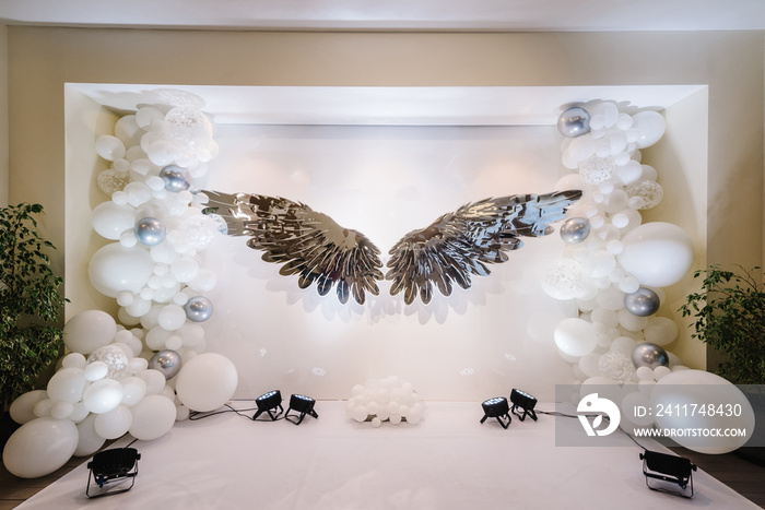 Photo zone with angel wings on the background of balloons. Photo area in silver style. Baby shower, newborn, birthday party concept design, decorations. Celebration baptism concept. Trendy decor.