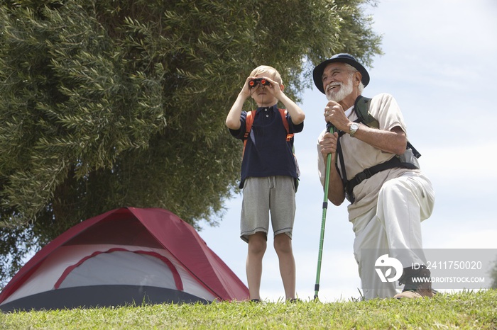 Grandfather and grandson with backpack bird watching in front of tent