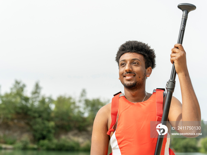 Portrait of young man wearing life jacket and holding oar