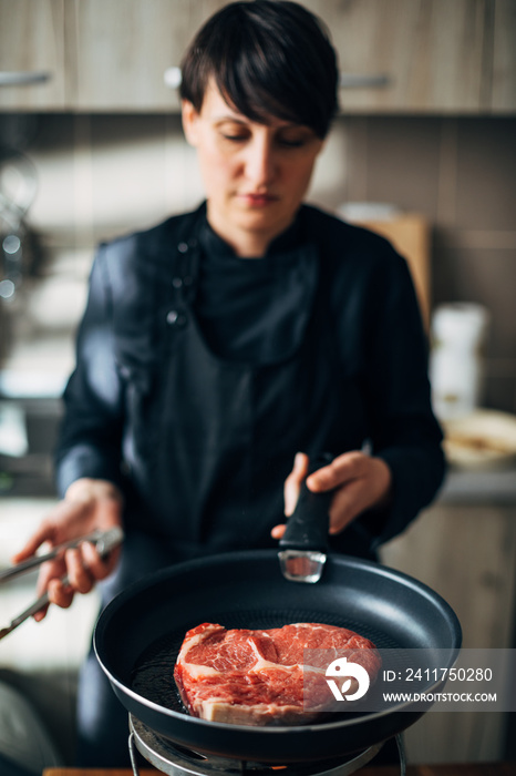 Chef frying ribeye steak in a pan