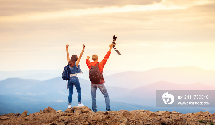 Happy travelers couple conquered top of mountain, raises hands up with camera and takes photos of landscapes on trip