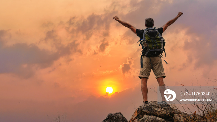 hiker with trekking stick hiking success on rocky hill top at sunset sky