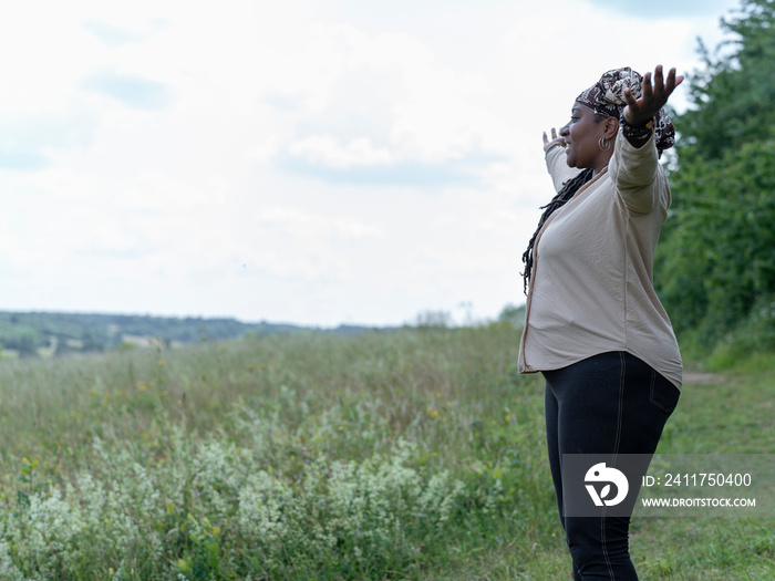 Mature woman standing in meadow with arms in air