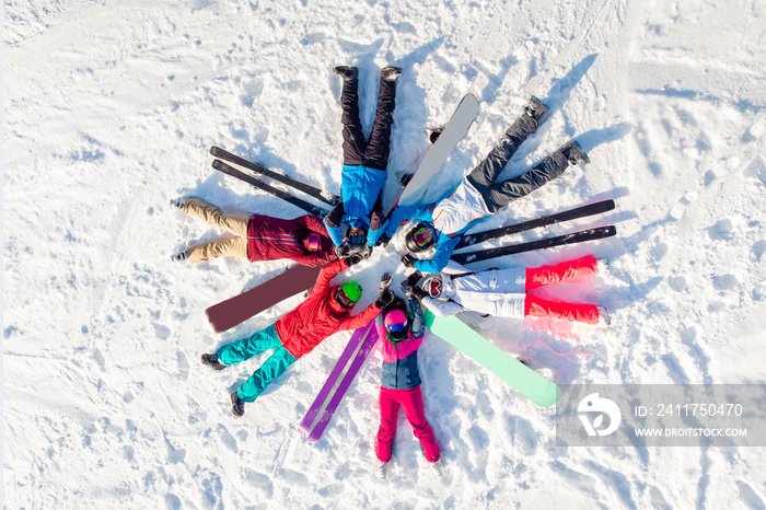 Happy team friends skiers and snowboarders having fun and lying circle on snow with snowboards and ski. Aerial top view