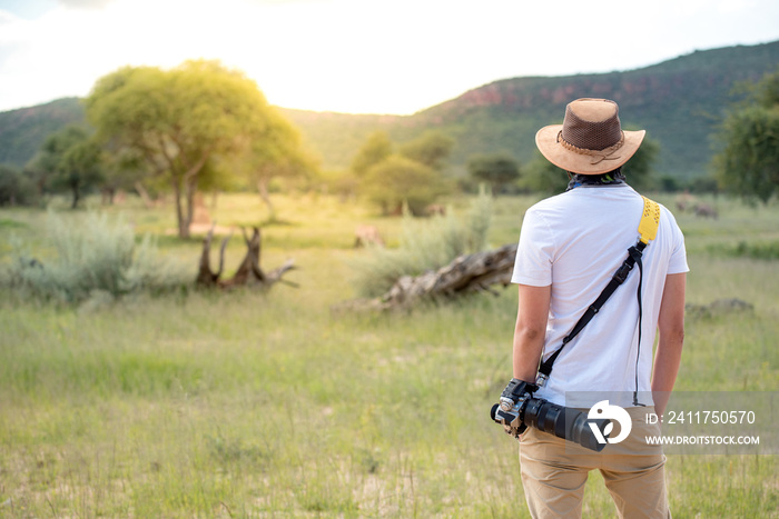 Young man traveler and photographer standing in safari looking at wildlife animals. Travel safari in Africa concept