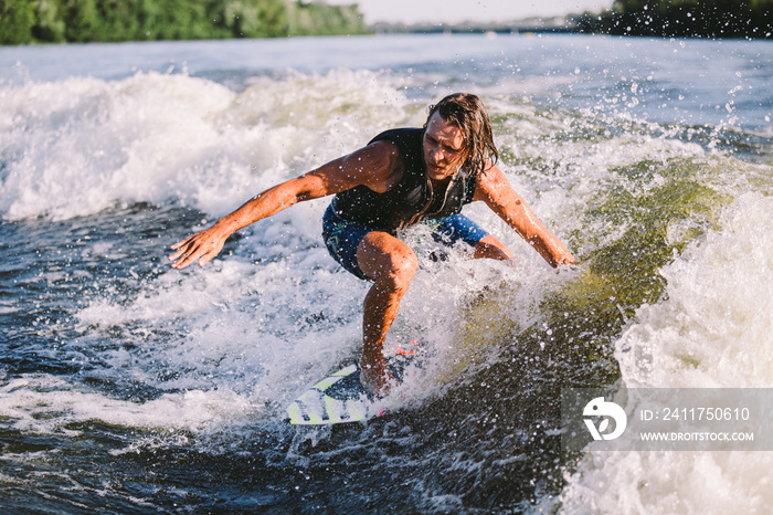 A man is surfing on a surfboard drawn by a motor boat above the wave of the boat. Weixerfer is engaged in surfing, entertainment, leisure, water sports. Athlete glides on the waves on the board