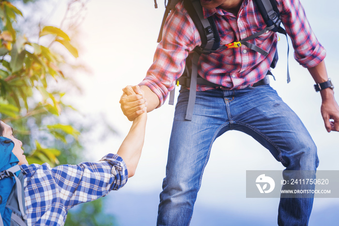 Young man with backpack helping friend to climb up to the top of mountain. select focus hands.