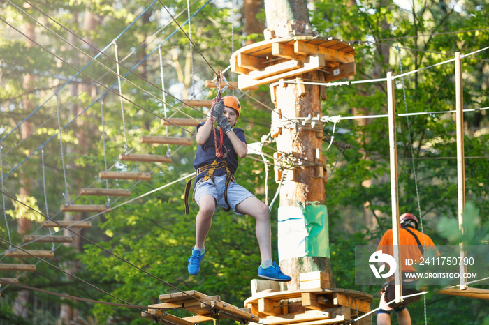 Sporty, young, cute boy in white t shirt spends his time in adventure rope park in helmet and safe equipment in the park in the summer. Active lifestyle concept