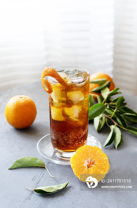 Chinotto drink in the glass with ice and fruits on the grey table