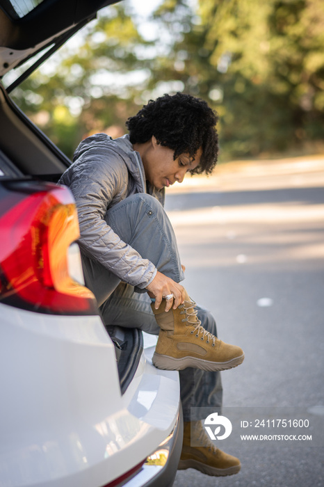 U.S. Army female soldier putting on combat boots and backpack before a hike.