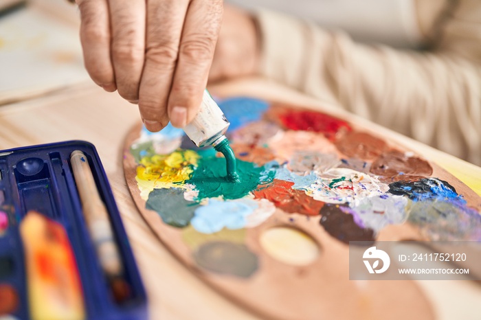 Middle age grey-haired man artist mixing color on palette at art studio