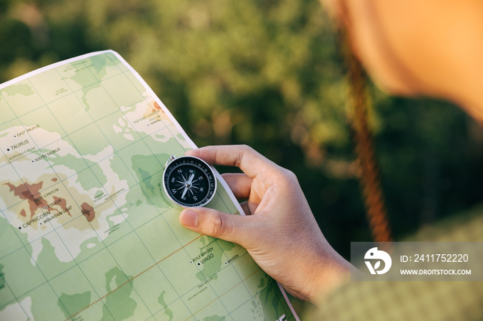 Asian teenager using compass with paoer map to hike through forest to peak of mountain.