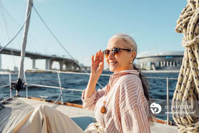 Beautiful senior woman holding a sunglasses and looking away on a private yacht