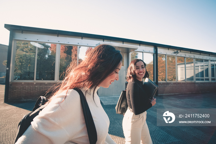 Couple of young woman student Of College Walking Through the campus. They walks trough university campus and laughing after meeting again at the university. Study together and learning concept. Trendy