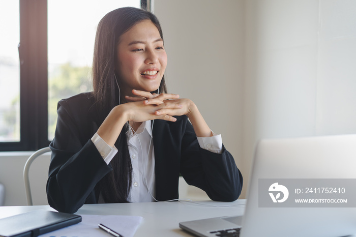 Working from home using internet communication concept. Asian young woman wear earphones talking  in video conference with business partners and worker team via online internet at her home.