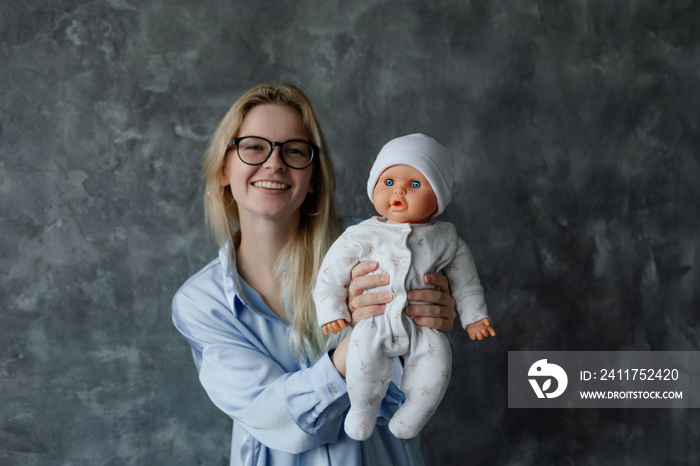 Smiling future mother take birth preparation course, gray wall background, free copy space. Successful mastering of practical skills of newborns care. Training for pregnant women, practice on doll